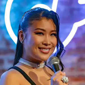 Comedian Jiaoying Summers poses on stage in front of the OnlyFans logo, with microphone, at LMAOF 109 in New York