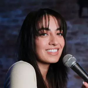 Comedian Irina Chelidze poses with a microphone in front of a brick wall