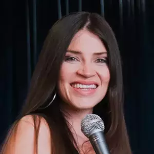 Comedian Katie Green poses on stage with a microphone.
