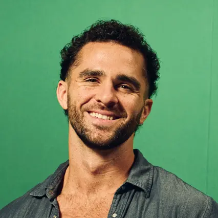 MarcoDelevecchio_updated Comedian Marco DelVecchio smiles and poses in front of a green background