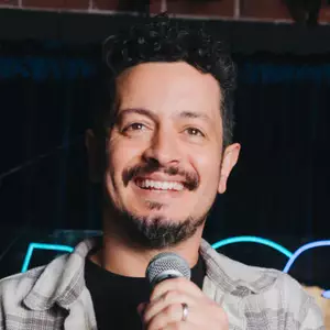 Comedian Zack Chapaloni poses in front of the OnlyFans logo.