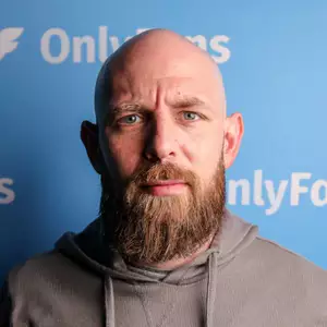 Comedian Jon Carden poses on stage in front of the LMAOF logo.