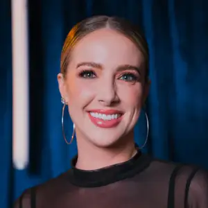 Comedian Brittany Schmitt smiles at the camera in front of a blue curtain