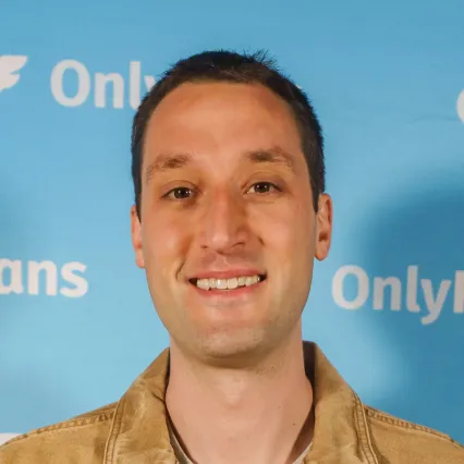 AlexDragicevich Comedian Alex Dragicevich poses in front of the OnlyFans logo at LMAOF.