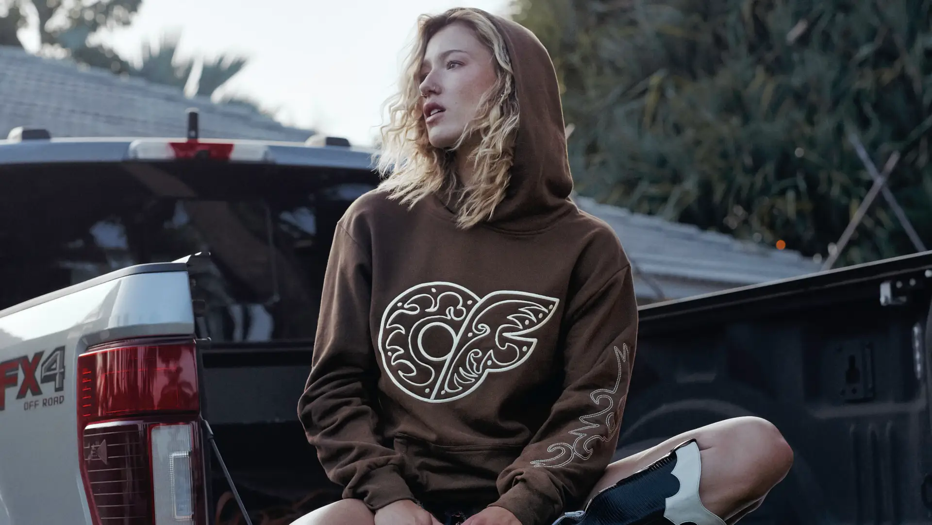 A model wears the Western Hoodie while sitting on the back of a pickup truck
