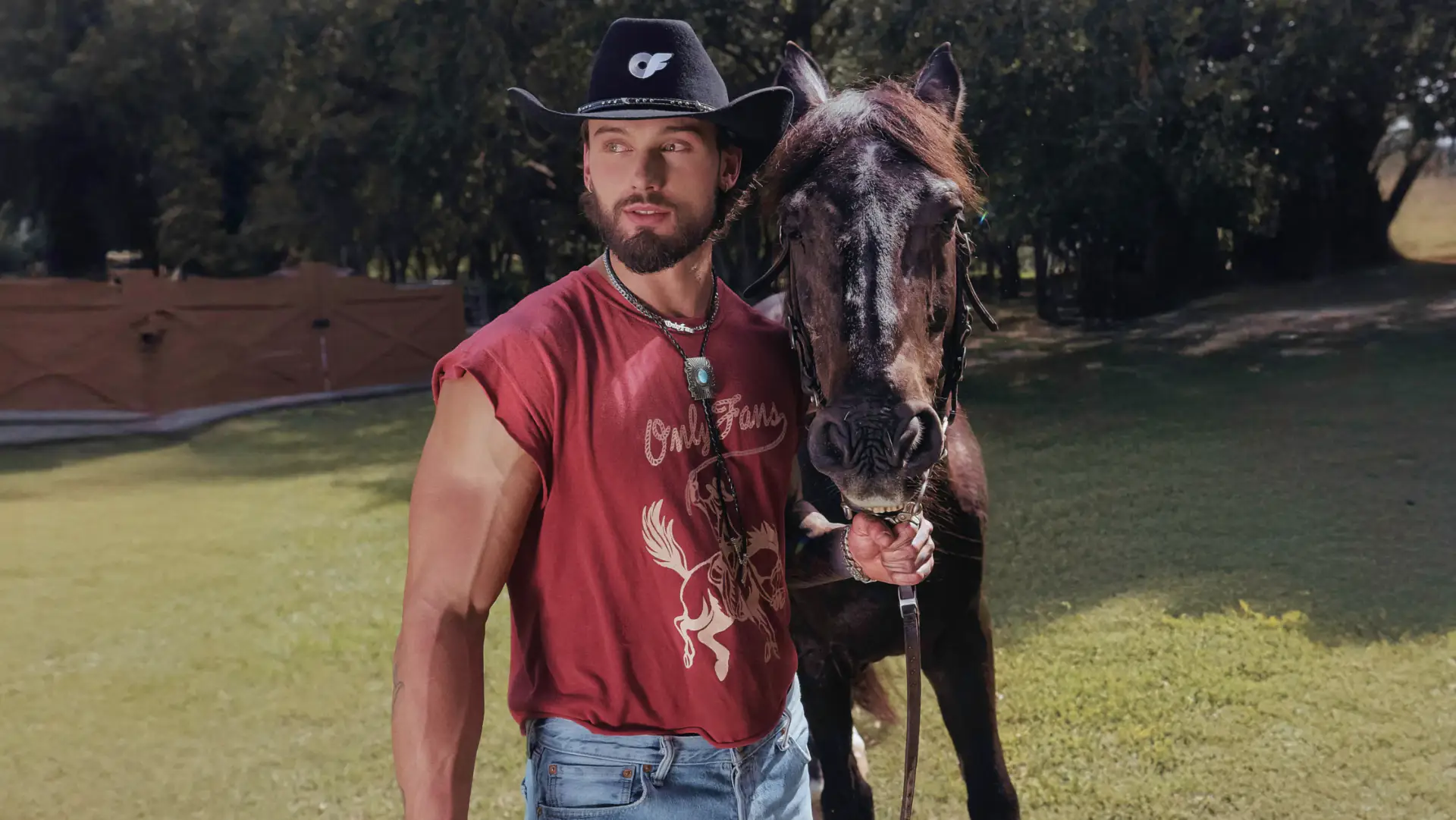 A male model wears the Cowboy Muscle Tee while guiding a horse