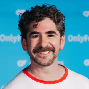 Josh Glanc smiles in front of an OnlyFans-branded blue step and repeat.