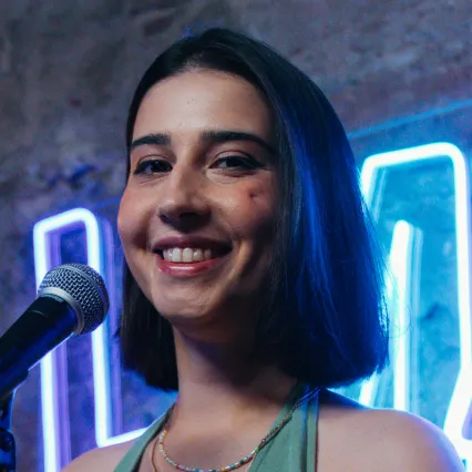 PriyaHall Priya Hall poses with a microphone in front of a neon OnlyFans sign on a brick wall.