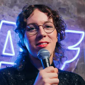 Sam Nicoresti poses on stage, holding a microphone.
