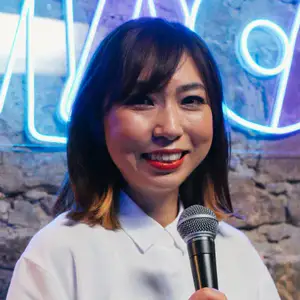Yurko Kotani poses with a microphone in front of a neon OnlyFans sign on a brick wall.