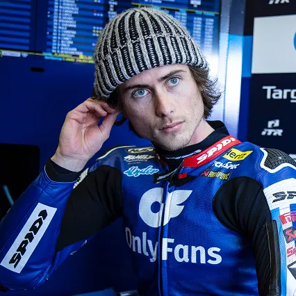 Joe Roberts sitting in the Moto2 garage wearing his OnlyFans American Racing Team suit and a knit beanie.