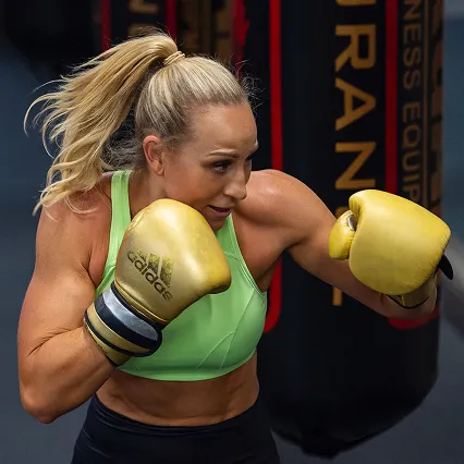 Australian boxer Kaye Scott trains in the gym, wearing gold gloves and a green sports top while throwing a punch.