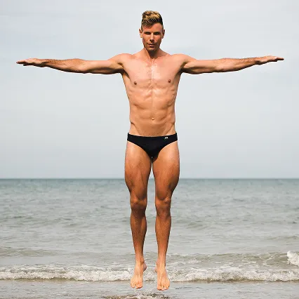 Robbie Manson, Olympic rower, jumps on the shores of a beach.