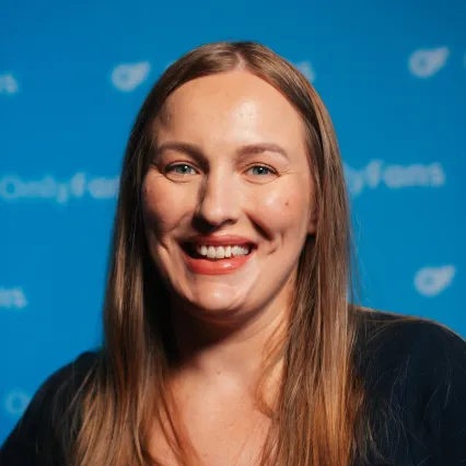 Tory Ward smiles in front of a blue backdrop with a repeating OnlyFans logo.