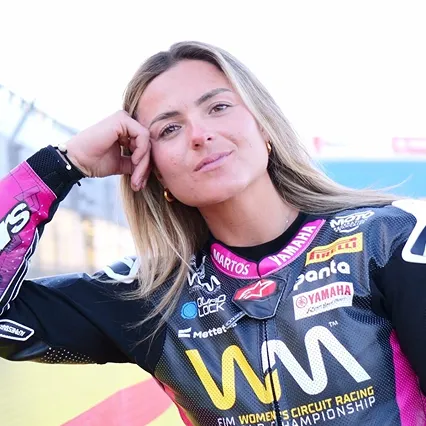 Emily Bondi in a Yamaha-branded motorcycle racing suit, posed trackside with her head resting on her hand, looking toward the camera.