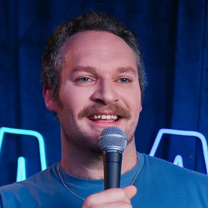 Matt LeGrande, comedian, performs on stage holding a microphone.