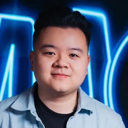 Will Pepper, comedian, smirks in front of a neon sign.