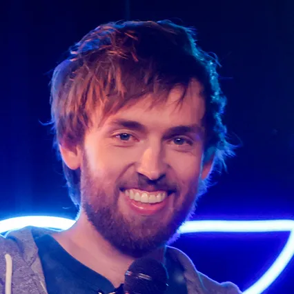 Stand-up comedian Collin Sledge holds a microphone and smiles.