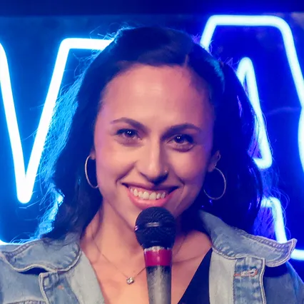 Stand-up comedian Sami Blumenthal holds a microphone and smiles.