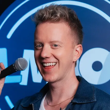 James Barr, comedian, poses with a microphone in front of the LMAOF logo.