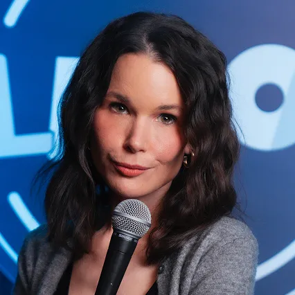 Michelle Shaughnessy, comedian, poses with a microphone in front of the LMAOF logo.