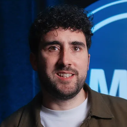 Steve Bugeja, comedian, smiles in front of the LMAOF logo.