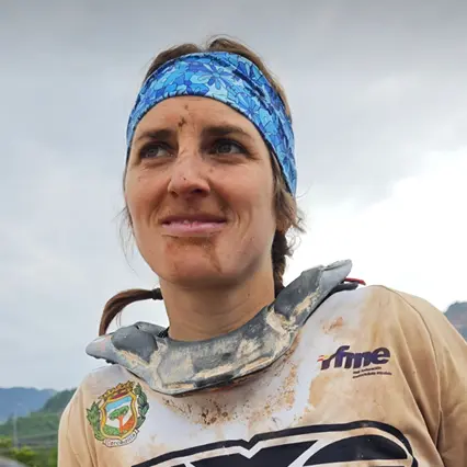 Sandra Gomez Sandra Gomez, professional motorsport rider, is covered in dirt in her racing uniform as she smirks off in the distance.