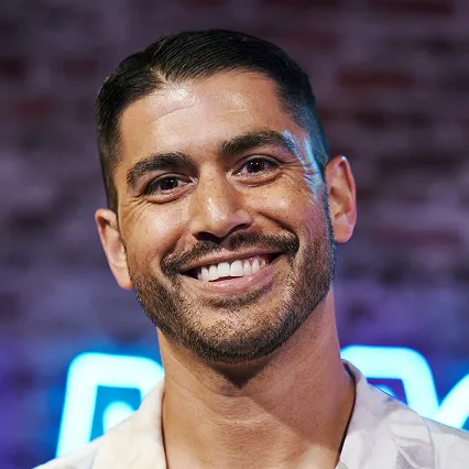 Smiling portrait of comedian Adam Mamawala in front of a blue neon LMAOF sign.