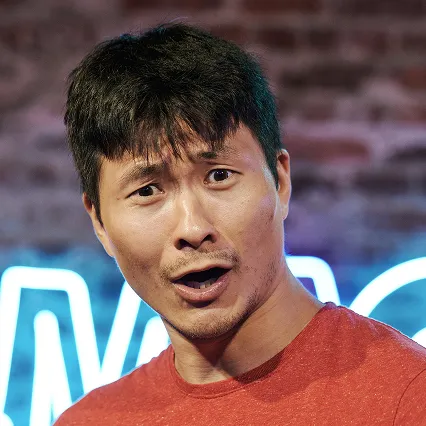 AlvinKuai Portrait of comedian Alvin with a surprised expression in front of a blue neon LMAOF sign.