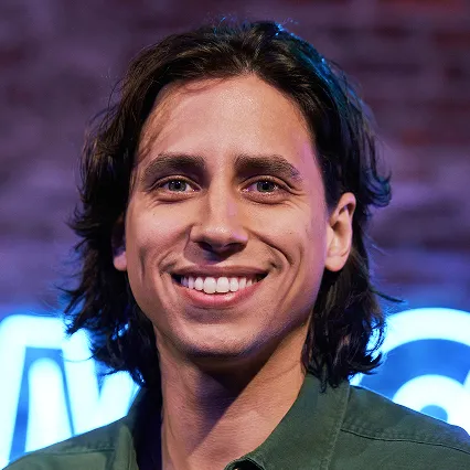LandoGonzalez Portrait of comedian Lando Gonzalez smiling in front of a blue neon LMAOF sign.