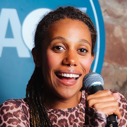 KateCheka British comedian Kate Cheka smiles while holding a microphone in front of an LMAOF backdrop.
