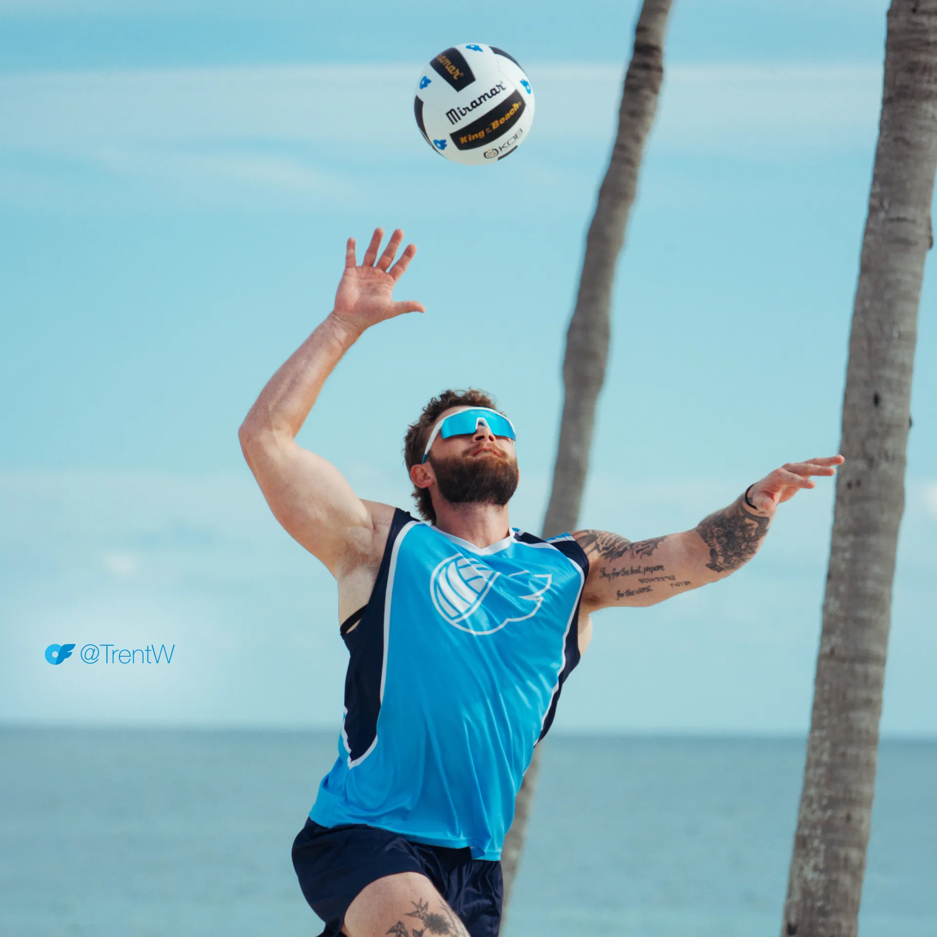 Trent_AllScreenSizes_1920x1920 Perfect Set winner Trent Williams tosses a volleyball overhead to serve on the beach in an OnlyFans jersey